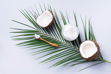 Coconut oil and ripe coconuts, tropical palm and monstera leaves on grey background with copy...