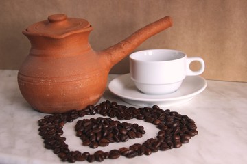 brown clay Turk, white clean Cup and saucer and roasted coffee beans in the shape of a heart on the...