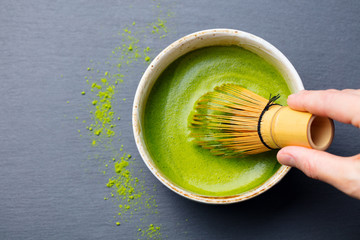 Matcha green tea cooking process in a bowl with bamboo whisk. Black slate background. Top view.