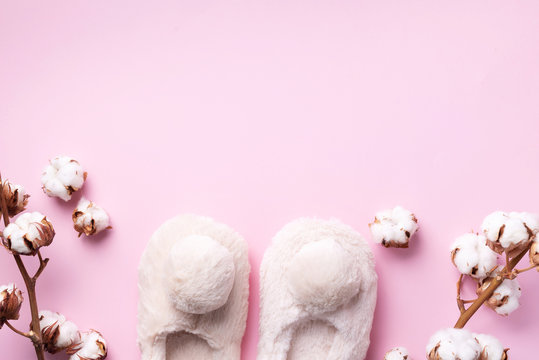 Nude fluffy home slippers with pompon and cotton flower branch on pink background with copy space. Top view. Copy space. Cozy home footwear. Sweet home and spa, body treatment concept