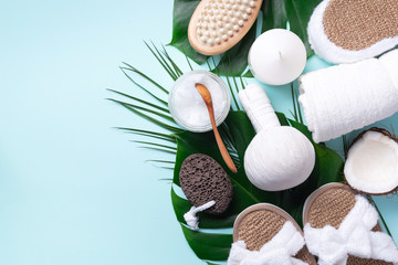 Spa, wwellness, skin care, beauty and relax concept. Spa tools: white towel, bamboo slippers, herbal ball, cream, wooden brush, coconut oil, monstera on blue background.