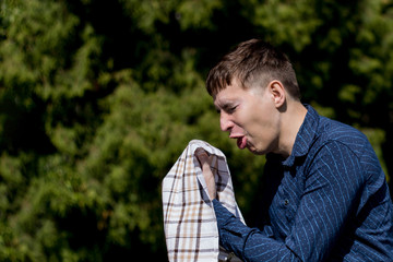 Closeup portrait of a young man with allergies. A man sneezes into a scarf on the background of...