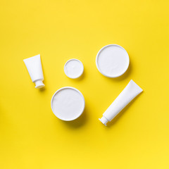 Cosmetics, skin care, beauty, body treatment concept. White cosmetic jar, tube, bottle and tropical monstera leaf over yellow background. Top view. Flat lay. Mock-up.