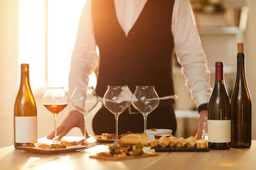 Mid section background of unrecognizable sommelier standing by table with wine bottles and snacks during tasting session lit by sunlight, copy space