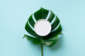 Moisturizing skin care cream on green monstera leaf over blue background with copy space. Top view....
