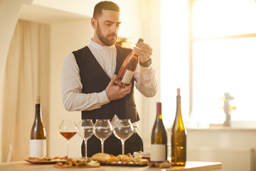 Waist up portrait of professional sommelier holding bottle of rose while preparing for wine tasting...