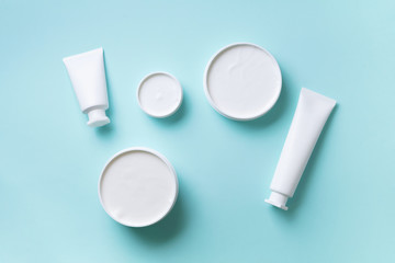 Cosmetics, skin care, beauty, body treatment concept. White cosmetic jar, tube, bottle and tropical monstera leaf over blue background. Top view. Flat lay. Mock-up.