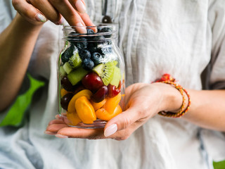 A glass jar with a salad of fruits and berries in the hands of a woman. Seasonal healthy healthy...