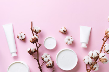 Fluffy cotton flowers, face cream, body butter on pink background with copy space. Cosmetics, beauty, spa concept. Top view. Flat lay