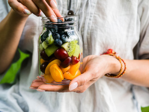 A glass jar with a salad of fruits and berries in the hands of a woman. Seasonal healthy healthy vegetarian food for a picnic