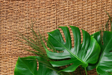 Green palm and tropical monstera leaves on rattan background. Bamboo texture. Natural, clean, fresh concept