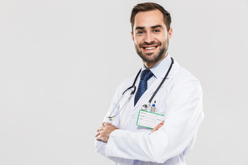 Portrait of cheerful young medical doctor with stethoscope smiling at camera and standing wth arms...