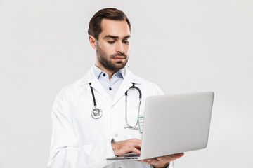 Portrait of caucasian young medical doctor with stethoscope working in clinic and holding laptop