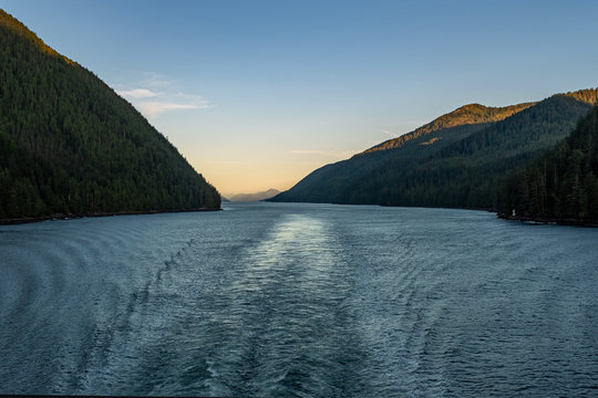 The view at sunset from the back of a ferry as it makes its way through the Inside Passage off the rugged west coast of Canada, the light fading behind the hills in the distance, nobody in the image