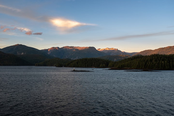 Naklejka na ściany i meble The view at sunset from the side of a ferry as it makes its way through the Inside Passage off the rugged west coast of Canada, the light fading behind the hills in the distance, nobody in the image