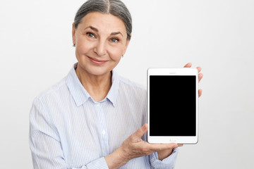 People, age and modern technology concept. Portrait of successful mature gray haired businesswoman in blue shirt holding generic digital tablet with blank copyspace display for your information