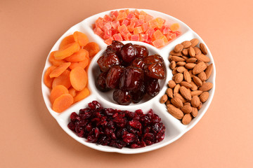 Mix of dried fruits and nuts on a white plate. Apricot, almond, raisin, dates fruit. On a brown background. Space for text or design.