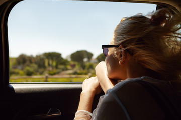 Back shot of attractive blonde European woman wearing sunglasses sitting inside car with open...