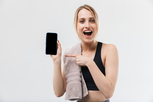 Image of pretty blond woman 20s dressed in sportswear with towel over neck using smartphone during workout in gym