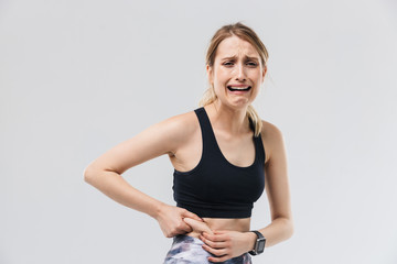 Image of upset blond woman 20s dressed in sportswear crying while touching her fat belly during workout in gym