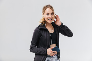 Image of beautiful blond woman 20s dressed in sportswear listening to music with headphones while running