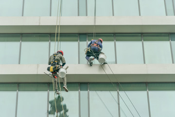 Two workers are washing the windows of a high-rise glass building. Work at heights, industrial mountaineering