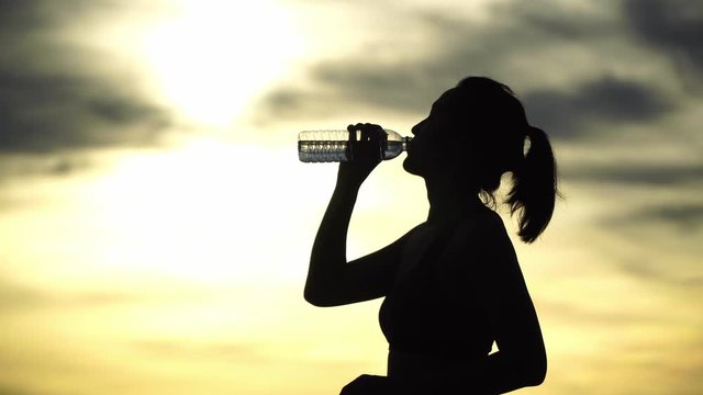 Silhouette. Women are drinking water after a refreshing workout. At sunset