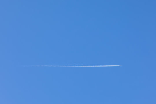 A High-resolution Image Of A Plane Flying Through The Clear Blue Sky Overhead, With A Trail Behind It. Mockup Template On The Topic Of Air Travel With Copy Space For Text.
