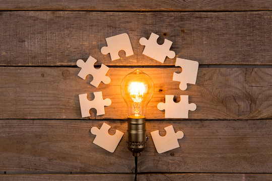 Idea and teamwork business concept, vintage incandescent light bulb and jigsaw on the wooden background