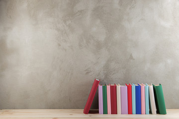 Education and reading concept - group of colorful books on the wooden table, concrete wall...