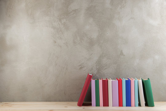 Education and reading concept - group of colorful books on the wooden table, concrete wall blackboard