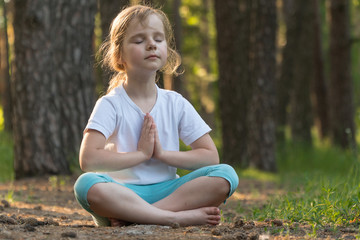 The child is practicing yoga in the forest.