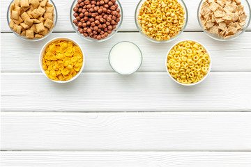Various corn cereals in bowls and milk on white wooden background top view copyspace