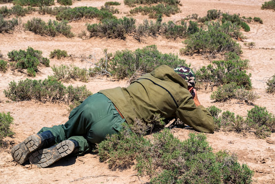 Back view outdoor photographer lies on ground taking picture of lizard in steppe