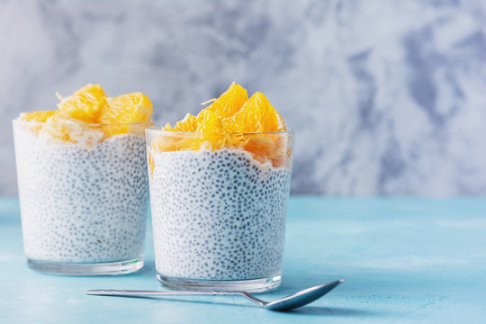 Greek Yogurt with Chia Seeds Healthy Vegan Meal. Tasty Homemade Dairy Smoothie Glass with Orange. Two Portions of Breakfast, Tablespoon on Table. Detox Food. Plant Based Diet Concept