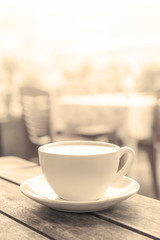 a white coffee mug stands on a wooden table in an outdoor coffee shop. light blurred background. close up, vertical photo