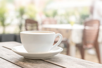 a white coffee mug stands on a wooden table in an outdoor coffee shop. light blurred background. close up