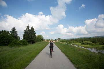 Young beautiful woman riding bicycle and spreading arms in countryside.