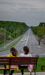 Two girls on a bench against the background of the road