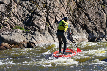 Sportsman paddling on rapids in whitewater river on a inflatable stand up paddle board (SUP)