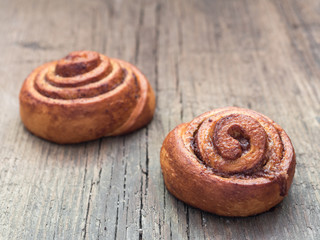 Confectionery baking. Sweet fresh soft roll bun with cinnamon on wooden background. Cinnabon closeup