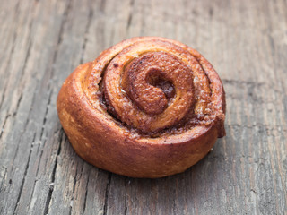 Confectionery baking. Sweet fresh soft roll bun with cinnamon on wooden background. Cinnabon closeup