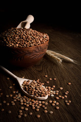 Lentil in a wooden bowl on a wooden background near the ears of wheat. wooden spoon with Lentil