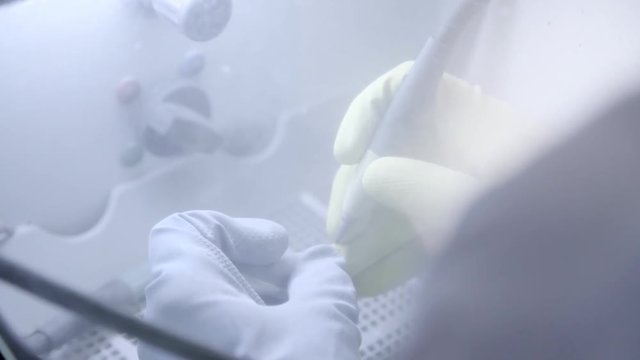 Dental technician polishing artificial ceramic teeth using sandblaster in the dental lab. Professional wearing gloves while holding fake teeth in hand and polishing it with sand blaster