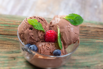 Chocolate ice cream balls with mint and raspberry close up and copy space on wooden background