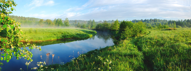 Sunny hazy panoramic landscape with small forest river at sunrise.
