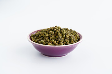 Dried green peppercorns in a violet bowl. White background, high resolution