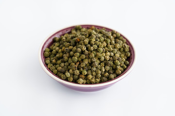 Dried green peppercorns in a violet bowl. White background, high resolution