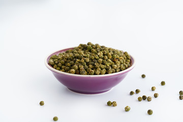 Dried green peppercorns in a violet bowl. White background, high resolution