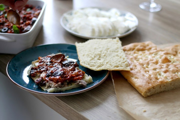 Preparing foccacia bread sandwich with pesto, porchetta meat, eggplant and tomato sauce, served with arugula and cherry tomato salad. Homemade italian cuisine. Selective focus.
